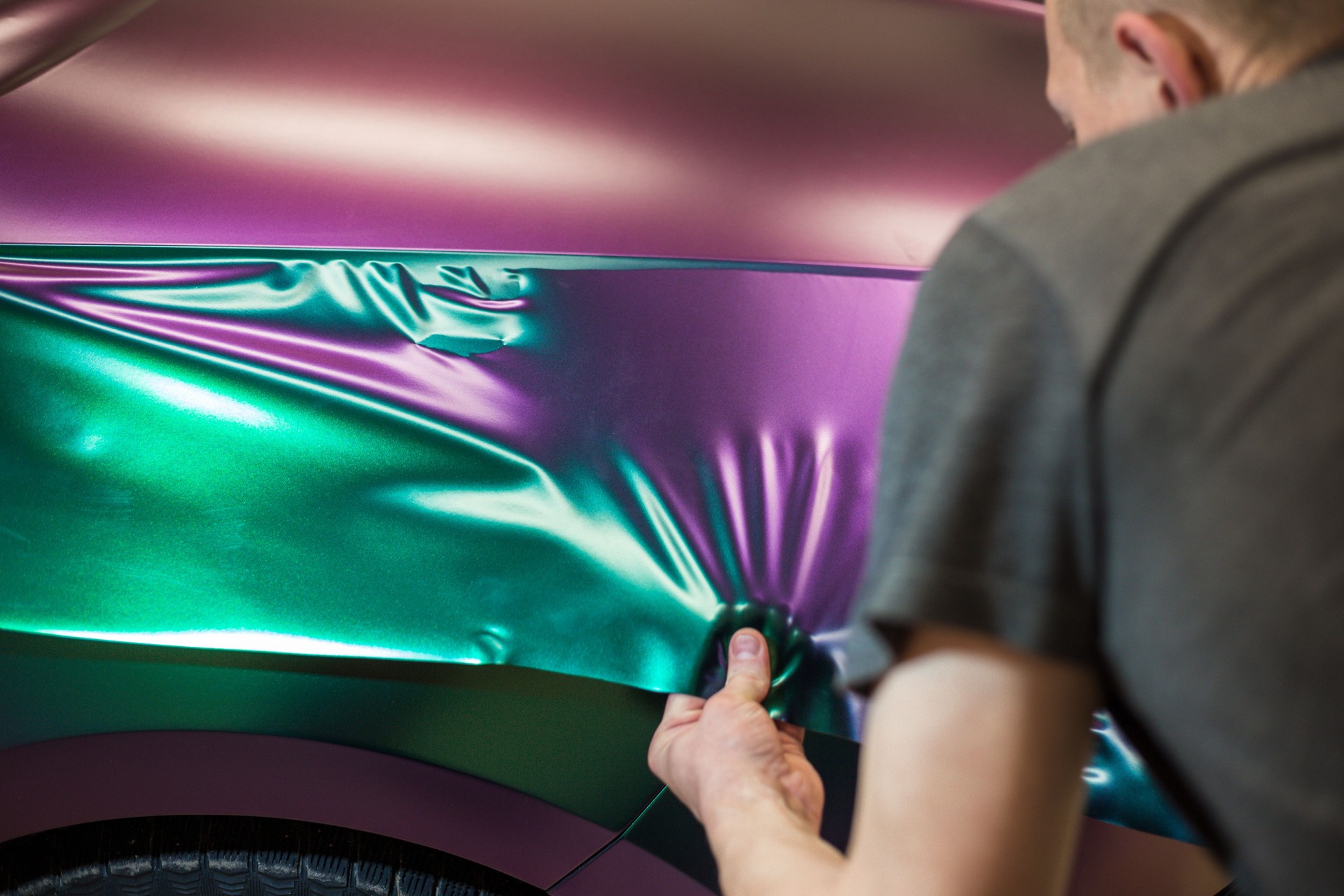 A specialist in wrapping a car with chameleon-colored vinyl film in the process of work. Car wrapping specialists cover the car with vinyl sheet or film.